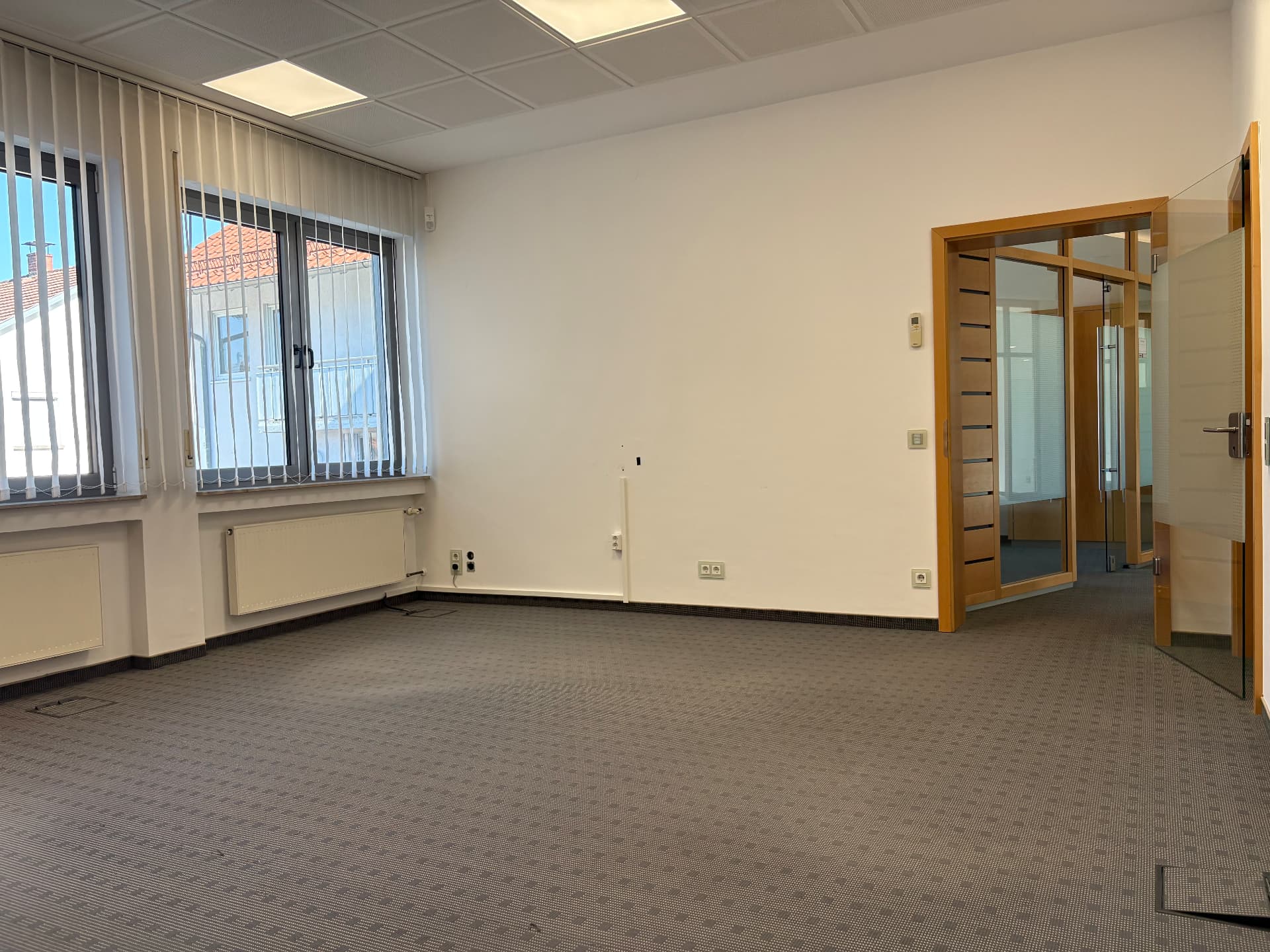 Fenster mit Vertikallamellen, Heizkörper, Teppichboden und Glas-Holz-Tür zum angrenzenden Bereich