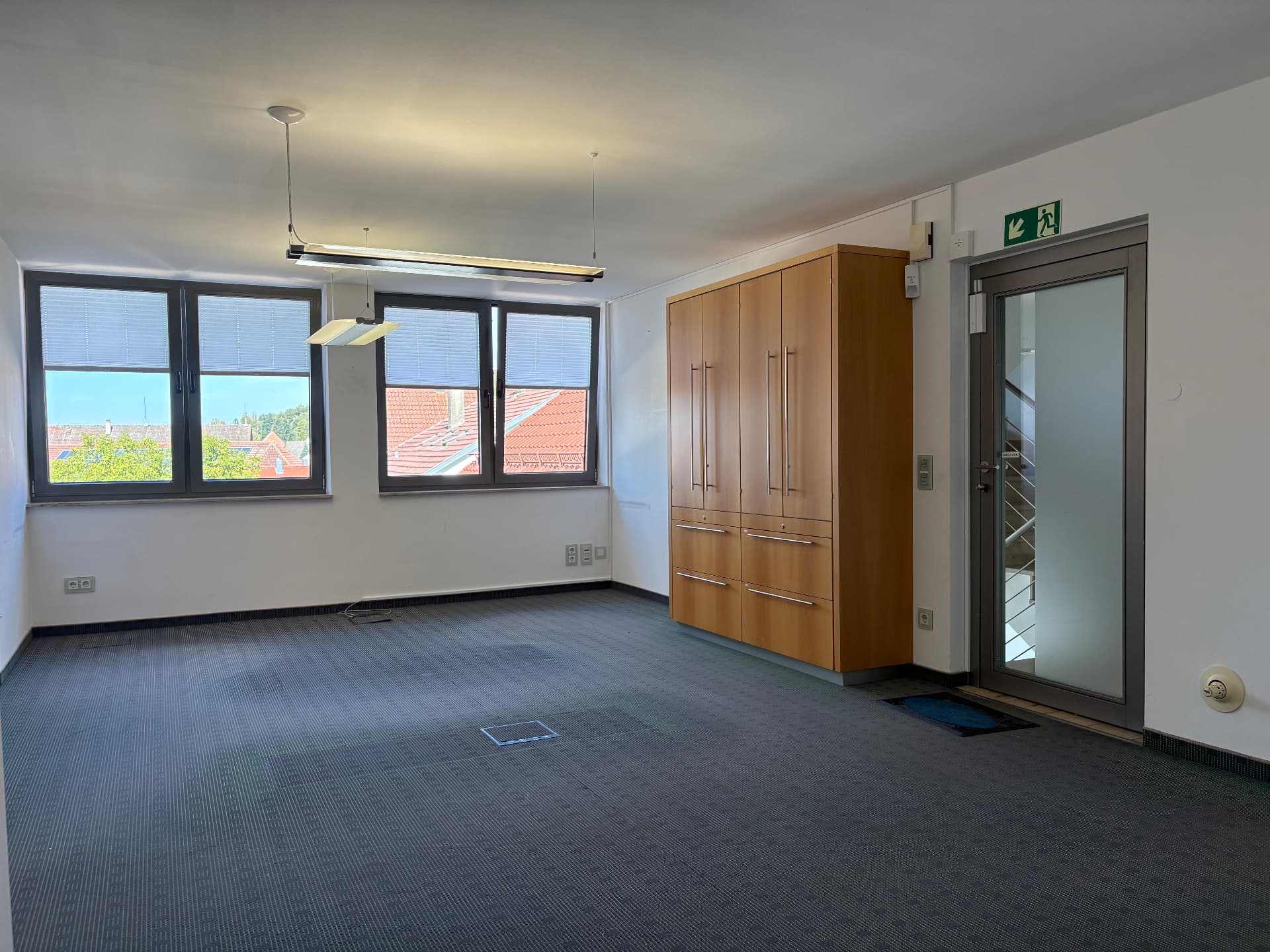 Breite Fensterfront, abgehängte Arbeitsplatzleuchten und Einbauschrank